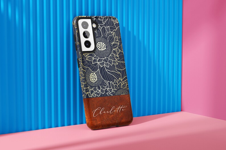 May include: A navy blue phone case with a gold sunflower design and a brown leather bottom with the name "Charlotte" written in white.