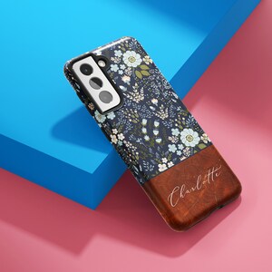 May include: A blue and white floral phone case with a brown leather bottom. The leather bottom has the name "Charlotte" written in white script.