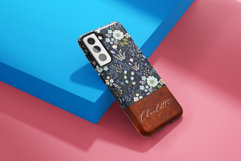 May include: A blue and white floral phone case with a brown leather bottom. The leather bottom has the name "Charlotte" written in white script.