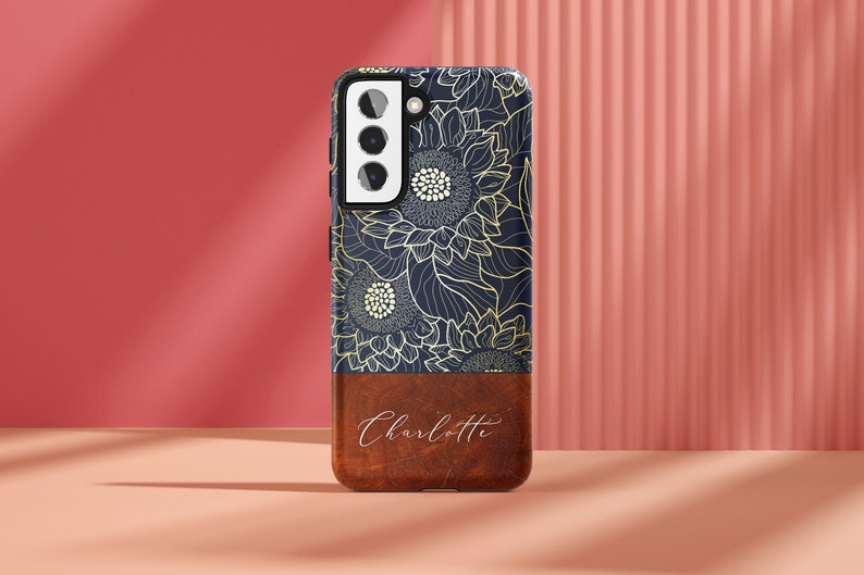 May include: A navy blue phone case with a gold sunflower design and a brown wood bottom with the name "Charlotte" engraved on it.