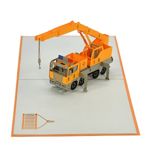 May include: A yellow and gray 3D pop-up card featuring a construction crane truck. The crane arm is extended and the hook is lowered. The card is open and the crane is standing on a gray background.