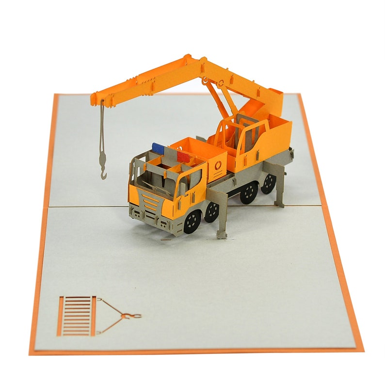 May include: A yellow and gray 3D pop-up card featuring a construction crane truck. The crane arm is extended and the hook is lowered. The card is open and the crane is standing on a gray background.