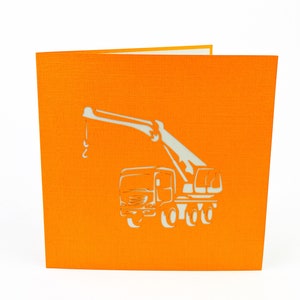 May include: Orange card with a white paper pop-up crane truck. The crane is extended and the truck has four wheels.