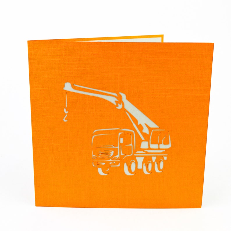 May include: Orange card with a white paper pop-up crane truck. The crane is extended and the truck has four wheels.