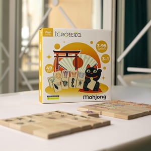 Può includere: Una scatola gialla con un'illustrazione di un gatto nero e il testo "Mahjong" sul davanti. La scatola contiene un gioco 3 in 1 con 49 pezzi in legno naturale. Il gioco è adatto per età dai 3 ai 99 anni.