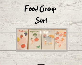 May include: A set of four educational cards labeled "Fruits", "Vegetable", "Dairy", and "Meats" with corresponding food illustrations. The words "Food Group Sort" are written in black script above the cards. A digital download icon is at the bottom.