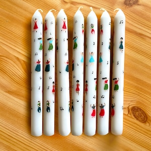 Peut inclure: Sept bougies blanches avec des motifs peints à la main de femmes dansant. Les femmes portent des robes colorées et sont entourées de notes de musique.