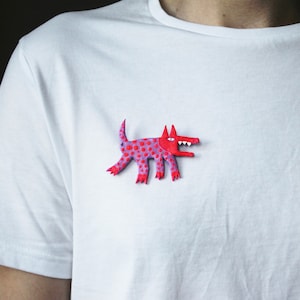 May include: A red and purple spotted dog brooch with a toothy grin. The brooch is made of polymer clay and is a whimsical and colorful accessory.