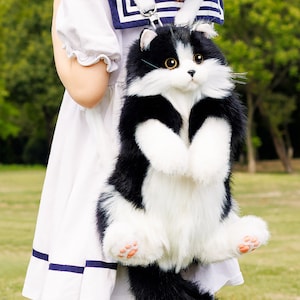 May include: A black and white plush cat backpack with a white face and black ears. The cat is sitting upright with its paws in the air.