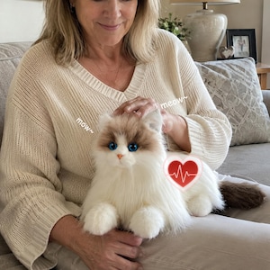 May include: A plush, lifelike cat toy with blue eyes, brown and white fur, and a brown tail. The toy has a red heart symbol with a heartbeat graphic and the word "meow" written on it.