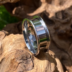 Puede incluir: Un anillo de plata con una banda ancha y un borde biselado. El anillo está hecho de metal y tiene un acabado pulido.