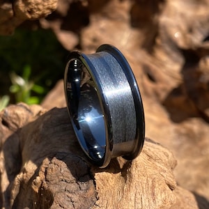 May include: A black tungsten carbide ring with a brushed finish and a beveled edge. The ring is shown on a piece of wood.