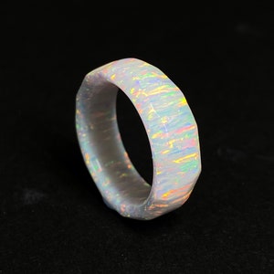 Op de afbeelding: Een witte opaalring met een facetgeslepen, geometrisch ontwerp. De opaal heeft een regenboogkleurige glans.