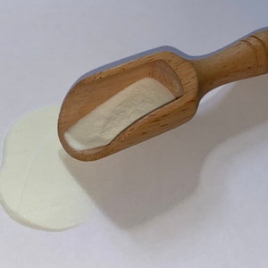 May include: A wooden scoop with a white powder spilling out onto a white surface.