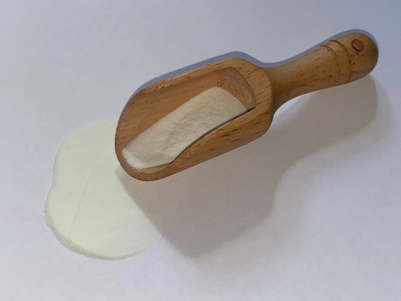 May include: A wooden scoop with a white powder spilling out onto a white surface.