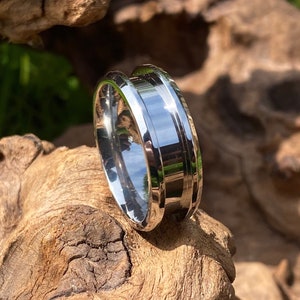 May include: A silver ring with a bevelled edge and a grooved design. The ring is made of metal and has a polished finish.