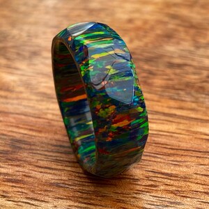 May include: A multi-colored ring with a faceted design. The ring is made of a dark blue, green, and orange material with a glossy finish.