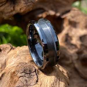 Puede incluir: Un anillo de carburo de tungsteno negro con acabado cepillado y borde biselado. El anillo tiene una incrustación negra.