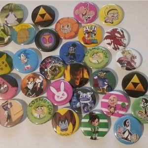 May include: A collection of 25 round button pins featuring various cartoon characters, including SpongeBob SquarePants, Sonic the Hedgehog, Pikachu, and characters from the video game "The Legend of Zelda".