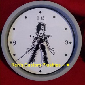 May include: A white clock face with black numbers and hands. The clock face features a pixelated image of a character from the video game Undertale. The clock face also has the text "Ren's Custom Plushies ~ ♥".