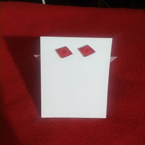 May include: A pair of red diamond-shaped earrings with a small circle in the center.