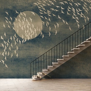 May include: A room with a mural depicting a flock of birds flying towards a large, pale circle against a dark blue background. A staircase with black railings and light-colored steps ascends along the wall. The floor is light-colored wood.