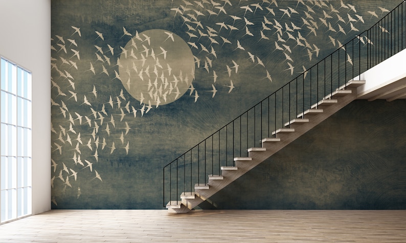 May include: A room with a mural depicting a flock of birds flying towards a large, pale circle against a dark blue background. A staircase with black railings and light-colored steps ascends along the wall. The floor is light-colored wood.