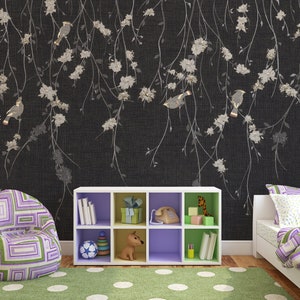 May include: A black and white floral wallpaper with a white bookshelf with purple shelves and a toy dog, a purple and green beanbag chair, and a white bed with a purple and green patterned comforter.
