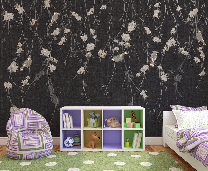 May include: A black and white floral wallpaper with a white bookshelf with purple shelves and a toy dog, a purple and green beanbag chair, and a white bed with a purple and green patterned comforter.