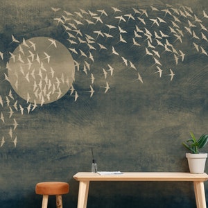 May include: A wallpaper mural featuring a flock of birds in flight against a dark blue and beige background. A large, pale circle suggests a moon or sun. A wooden table and a potted plant are in the foreground.