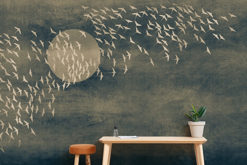 May include: A wallpaper mural featuring a flock of birds in flight against a dark blue and beige background. A large, pale circle suggests a moon or sun. A wooden table and a potted plant are in the foreground.