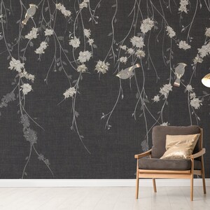May include: A dark gray wallpaper with a delicate floral pattern and gold birds. A brown armchair with a gold throw pillow sits in front of the wallpaper. A gold floor lamp with a white shade is in the corner.