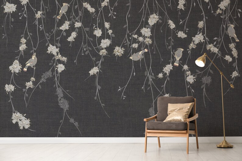 May include: A dark gray wallpaper with a delicate floral pattern and gold birds. A brown armchair with a gold throw pillow sits in front of the wallpaper. A gold floor lamp with a white shade is in the corner.