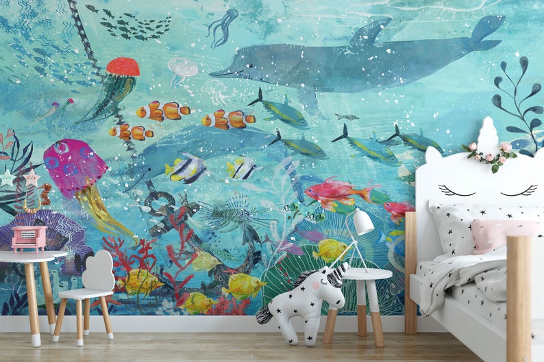 May include: A colorful underwater scene with a dolphin, jellyfish, and various fish. The scene is painted on a wall in a child's bedroom with a white unicorn-shaped headboard and a white stuffed unicorn on the floor.