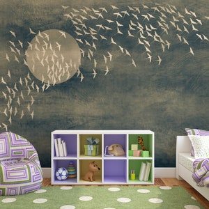 May include: A child's bedroom with a mural of a full moon and flying birds. The room features a patterned beanbag chair, a white cube shelf with toys and books, a bed with purple bedding, and a green polka-dot rug.