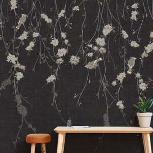 May include: A black and white floral wallpaper with gold birds. The wallpaper is hanging on a wall with a wooden table and a stool in front of it. There is a potted plant on the table.