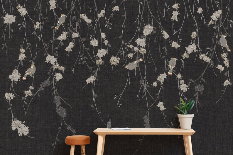 May include: A black and white floral wallpaper with gold birds. The wallpaper is hanging on a wall with a wooden table and a stool in front of it. There is a potted plant on the table.