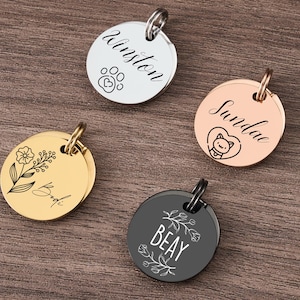 May include: Four personalized pet ID tags in silver, gold, rose gold, and black. Each tag is round with a ring for attachment. The tags feature engraved names, paw prints, floral designs, and a cat illustration.