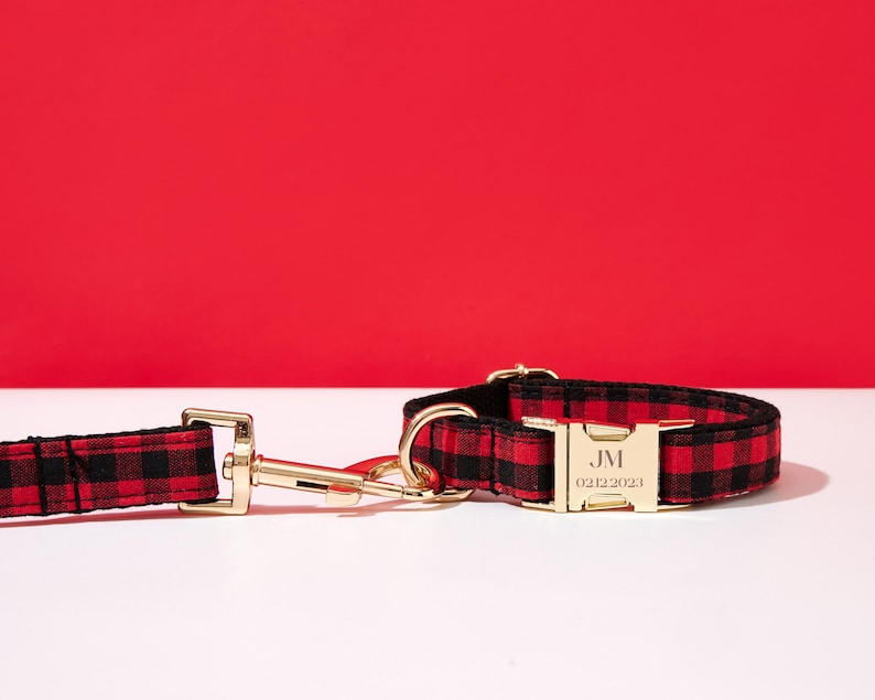 May include: Red and black buffalo plaid dog collar with a gold buckle and a personalized tag that reads "JM 02/12/2023".