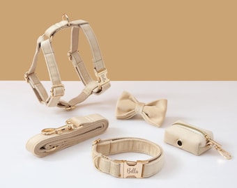 Puede incluir: Un arnés, una correa, un collar y un porta bolsas para excrementos para perro de color beige con herrajes dorados. El collar y el arnés tienen el nombre "Bella" grabado.