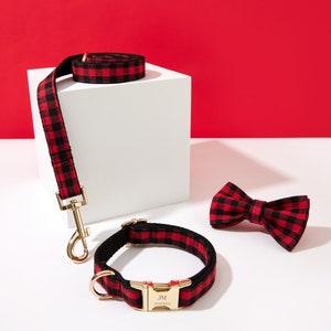 May include: Red and black plaid dog collar and leash set with a matching bow tie. The collar has a gold buckle with the text "JM" engraved on it.