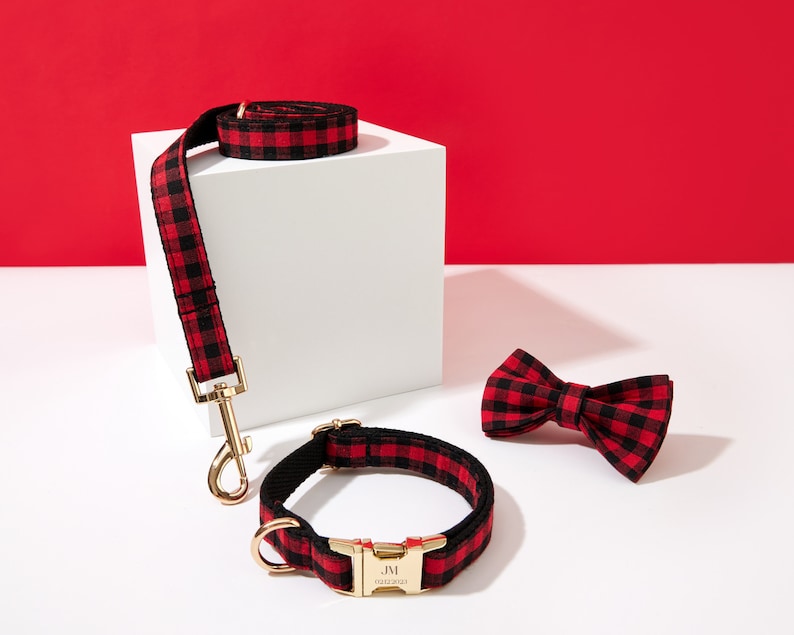May include: Red and black plaid dog collar and leash set with a matching bow tie. The collar has a gold buckle with the text "JM" engraved on it.
