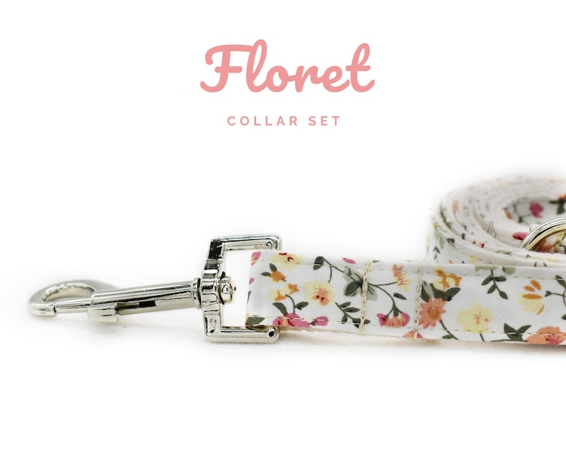 K&ouml;nnte beinhalten: Ein wei&szlig;es Hunde-Halsband- und Leinen-Set mit Blumenmuster und einem silbernen Metallverschluss und Haken. Leine und Halsband zeigen ein Muster aus kleinen gelben, rosa und orangefarbenen Blumen. Der Text "Floret COLLAR SET" ist in Rosa geschrieben.
