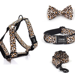 Pode incluir: Um conjunto de arnês, coleira, trela e gravata borboleta para cão com estampa de leopardo. A coleira tem uma fivela preta com o nome "EDDIE" e o número de telefone "700 139 88 11" impressos nela.