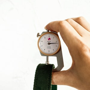 May include: A close-up of a metal caliper measuring a dark green fabric strap. The caliper reads 0.1mm 0-10mm and is labeled MINPAI.