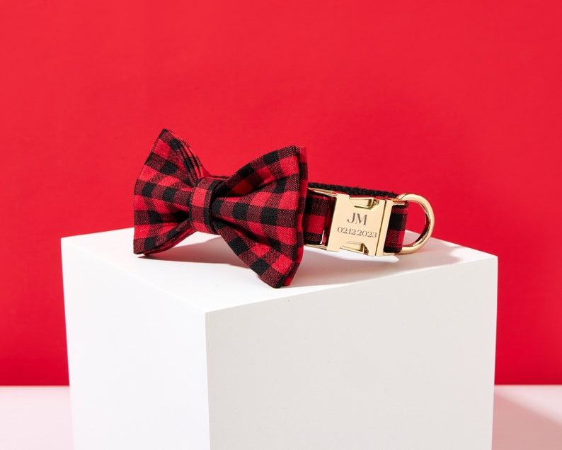 May include: Red and black buffalo plaid bow tie dog collar with a gold buckle engraved with "JM 02.12.2023".