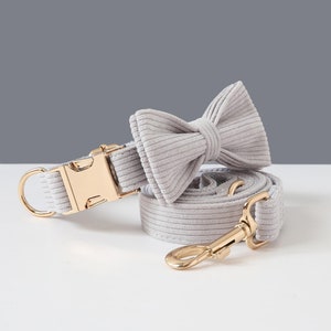 May include: A light gray corduroy dog collar, leash, and bow tie set. The collar features a gold-colored metal buckle and a D-ring. The leash has a matching gold-colored metal clasp. The bow tie is pre-tied.