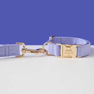 May include: A lavender corduroy dog collar and leash set with a gold buckle. The buckle has the name "Stella" and phone number "123-456-789" engraved on it.