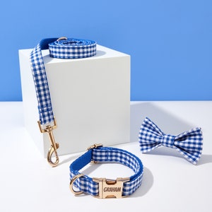 Puede incluir: Conjunto de collar y correa para perro de gingham azul y blanco con hebilla dorada y pajarita a juego. El collar tiene el nombre "GRAHAM" grabado en la hebilla.