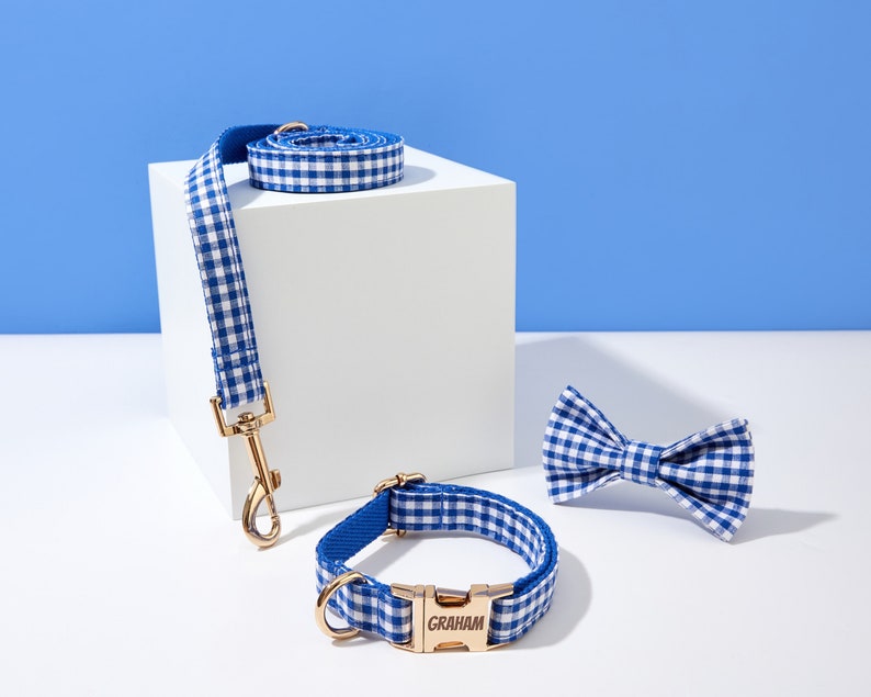 Puede incluir: Conjunto de collar y correa para perro de gingham azul y blanco con hebilla dorada y pajarita a juego. El collar tiene el nombre "GRAHAM" grabado en la hebilla.